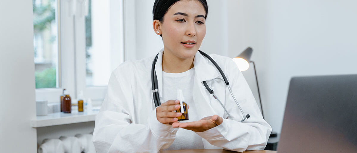 a female doctor holding a bottle of medicine in front of a laptop
